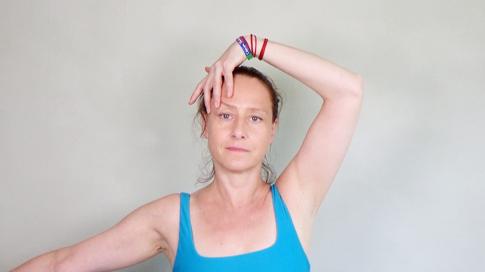 Hanna Sahlman practising Face Yoga, one arm raised with her fingertips resting on her forehead, looking directly at the camera.